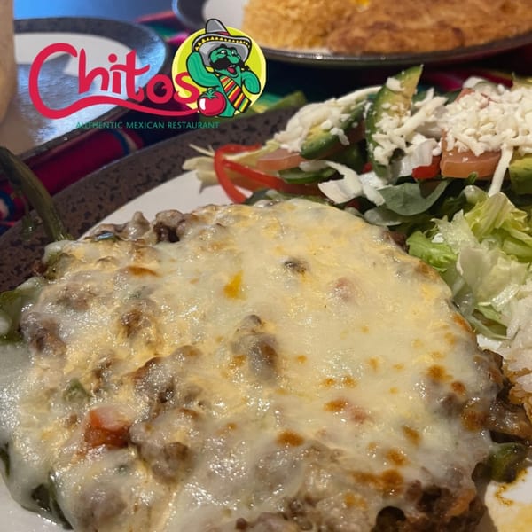 A close-up of a cheesy Mexican dish with a side salad and the Chitos restaurant logo.