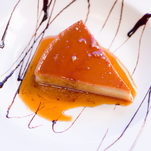 A slice of Chitos' flan dessert, drizzled with caramel sauce and chocolate on a white plate.