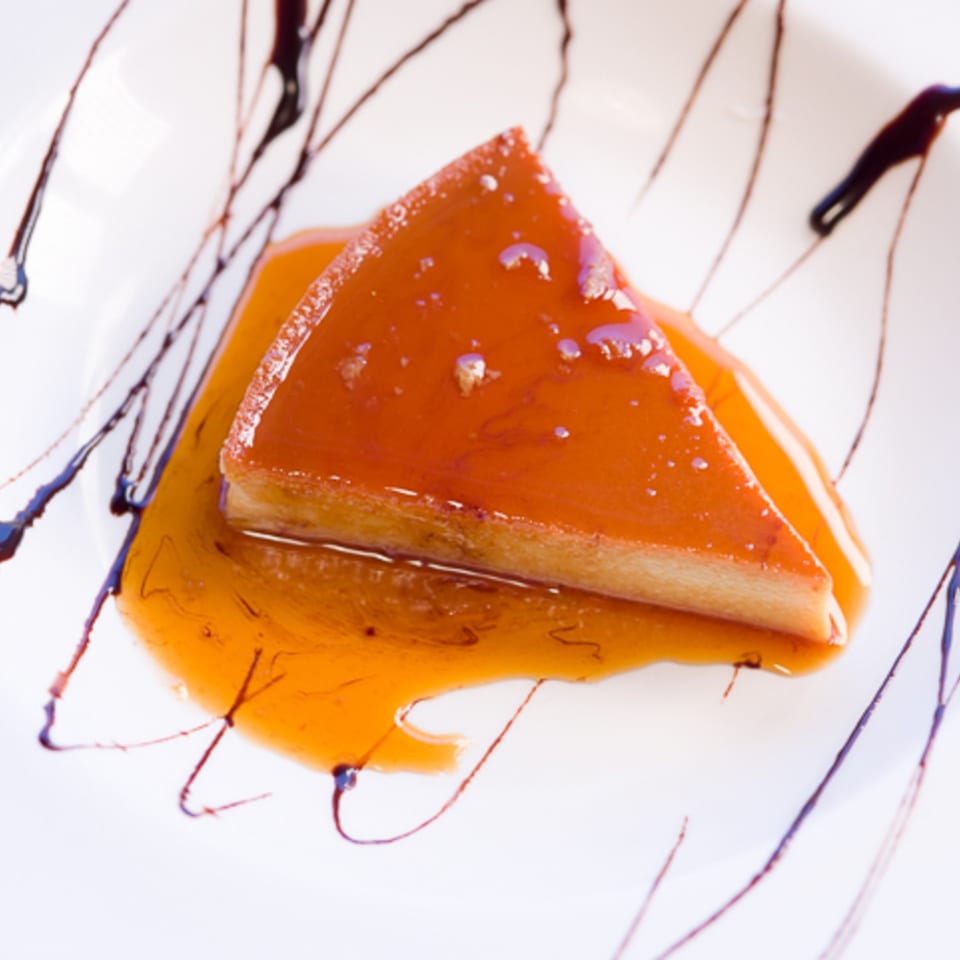 A slice of Chitos' flan dessert, drizzled with caramel sauce and chocolate on a white plate.