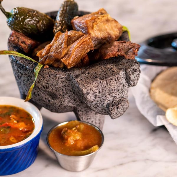 Chitos Mexican molcajete filled with grilled meat and jalapeños, with two bowls of salsa.