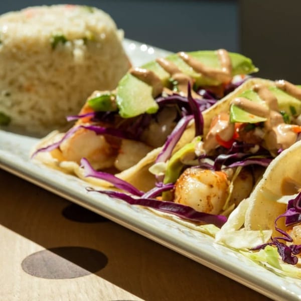 Shrimp tacos with red cabbage, avocado, and sauce, served with a side of rice.