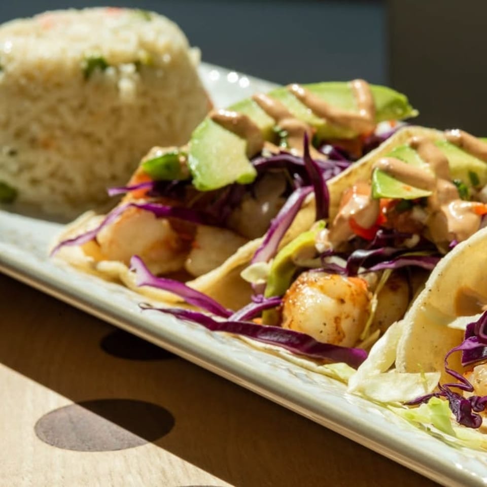 Shrimp tacos with red cabbage, avocado, and sauce, served with a side of rice.