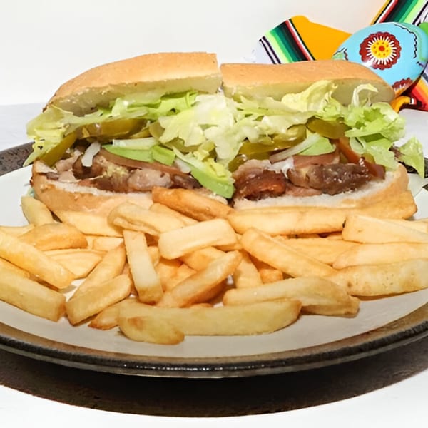 Two halves of a Mexican torta sandwich with meat, lettuce, and pickles, served with french fries.