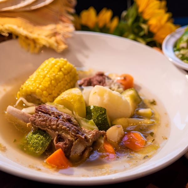 Hearty Mexican beef soup with corn, potatoes, carrots, and zucchini in a white bowl.