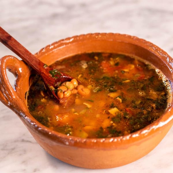 Hearty Mexican bean soup with vegetables and a wooden spoon in a rustic clay bowl.